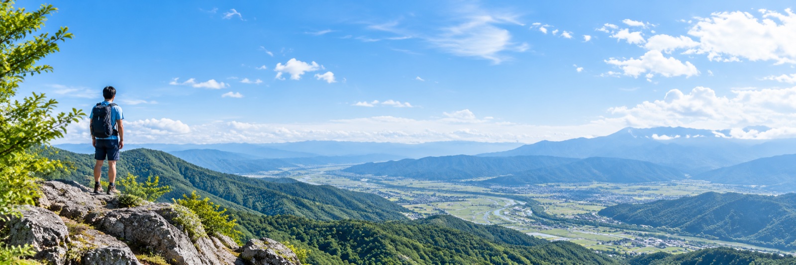 山の展望台から緑の谷と青空を見渡す人
